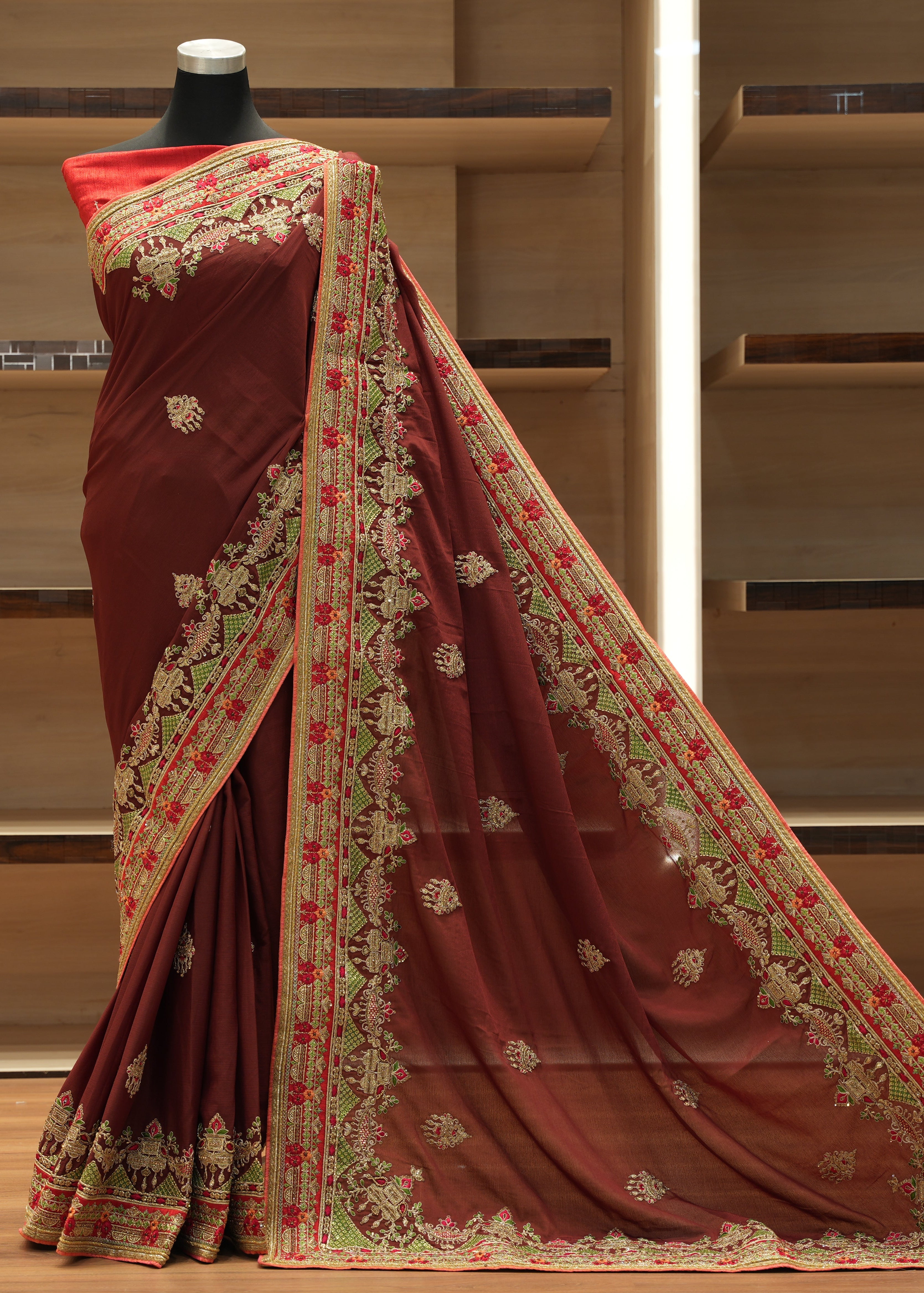 Maroon saree with gold and red embroidery on a mannequin against a wooden background