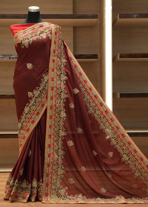 Maroon saree with gold and red embroidery on a mannequin against a wooden background