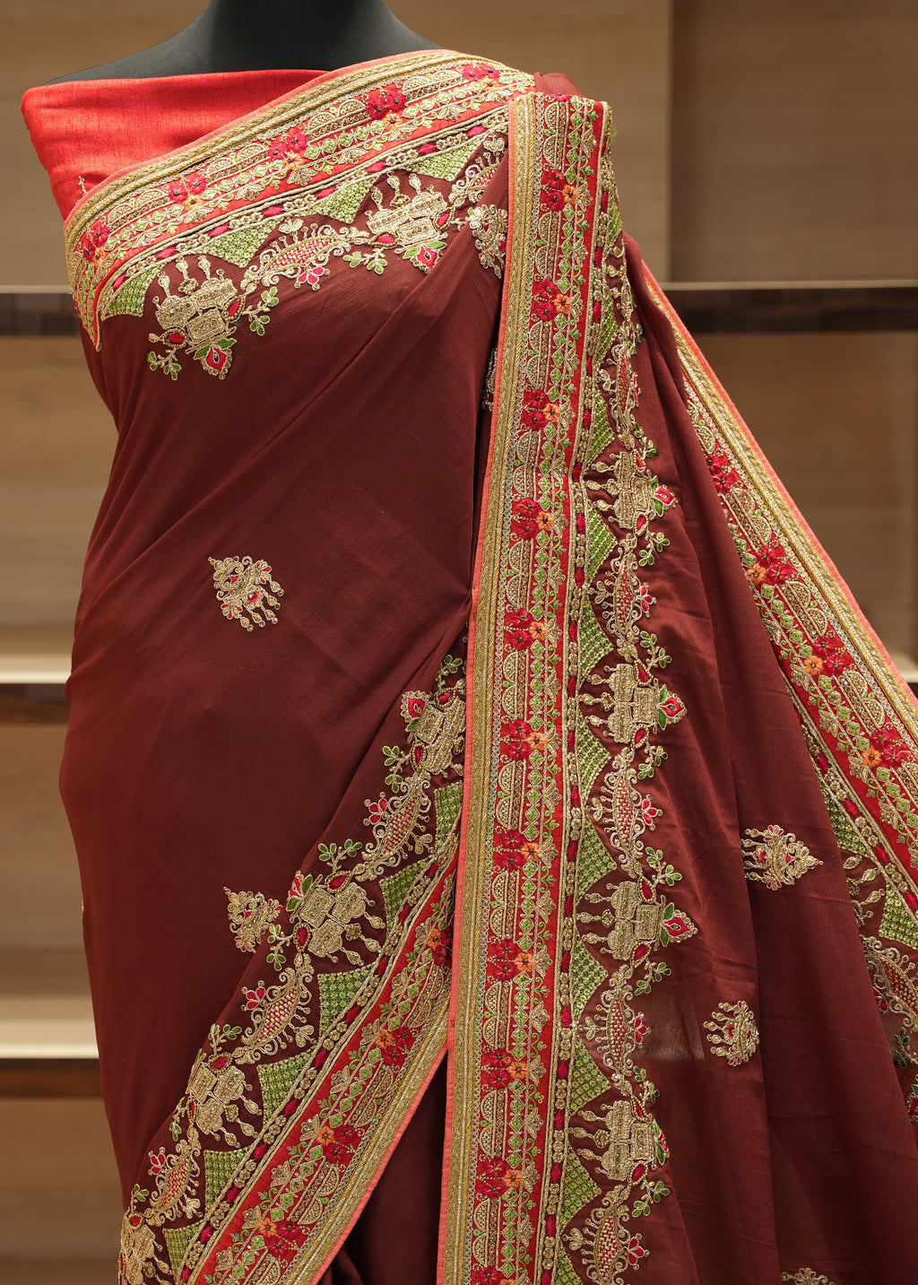 Maroon saree with intricate gold and red embroidery on a mannequin against a neutral background.
