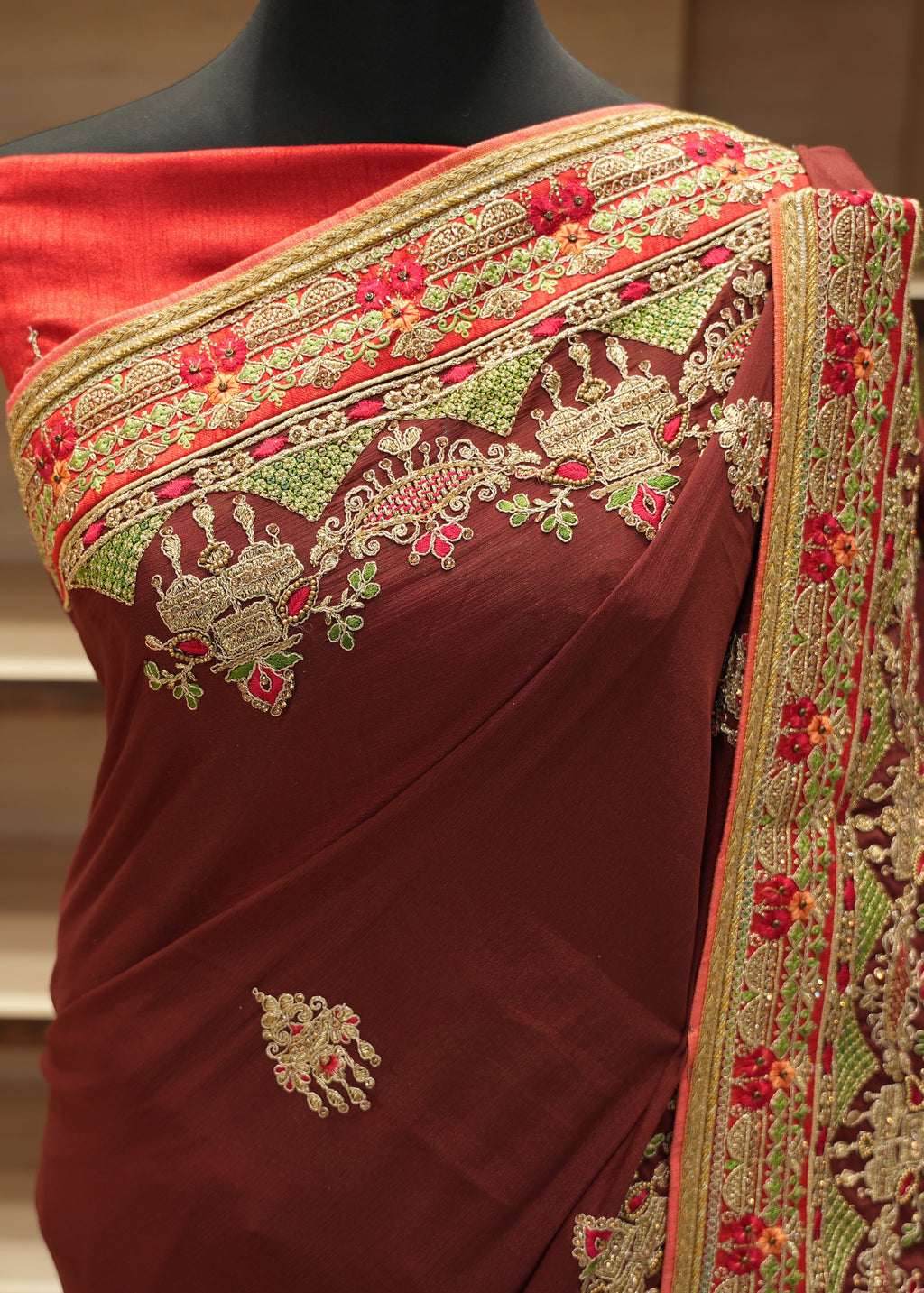Maroon saree with gold and red embroidery on a mannequin against a neutral background