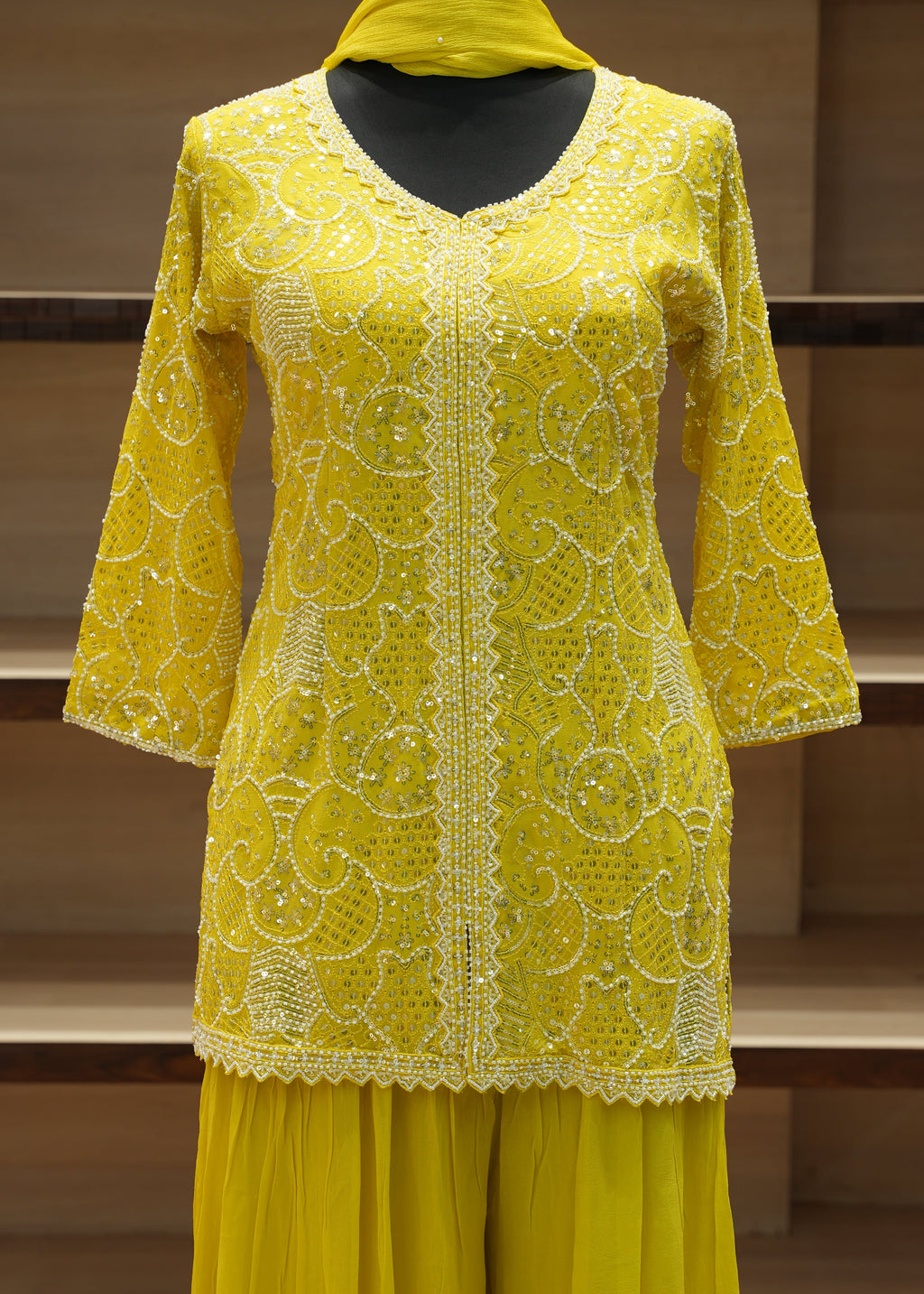 Yellow embroidered garment on a wooden stand against a neutral background