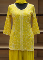 Yellow embroidered garment on a wooden stand against a neutral background