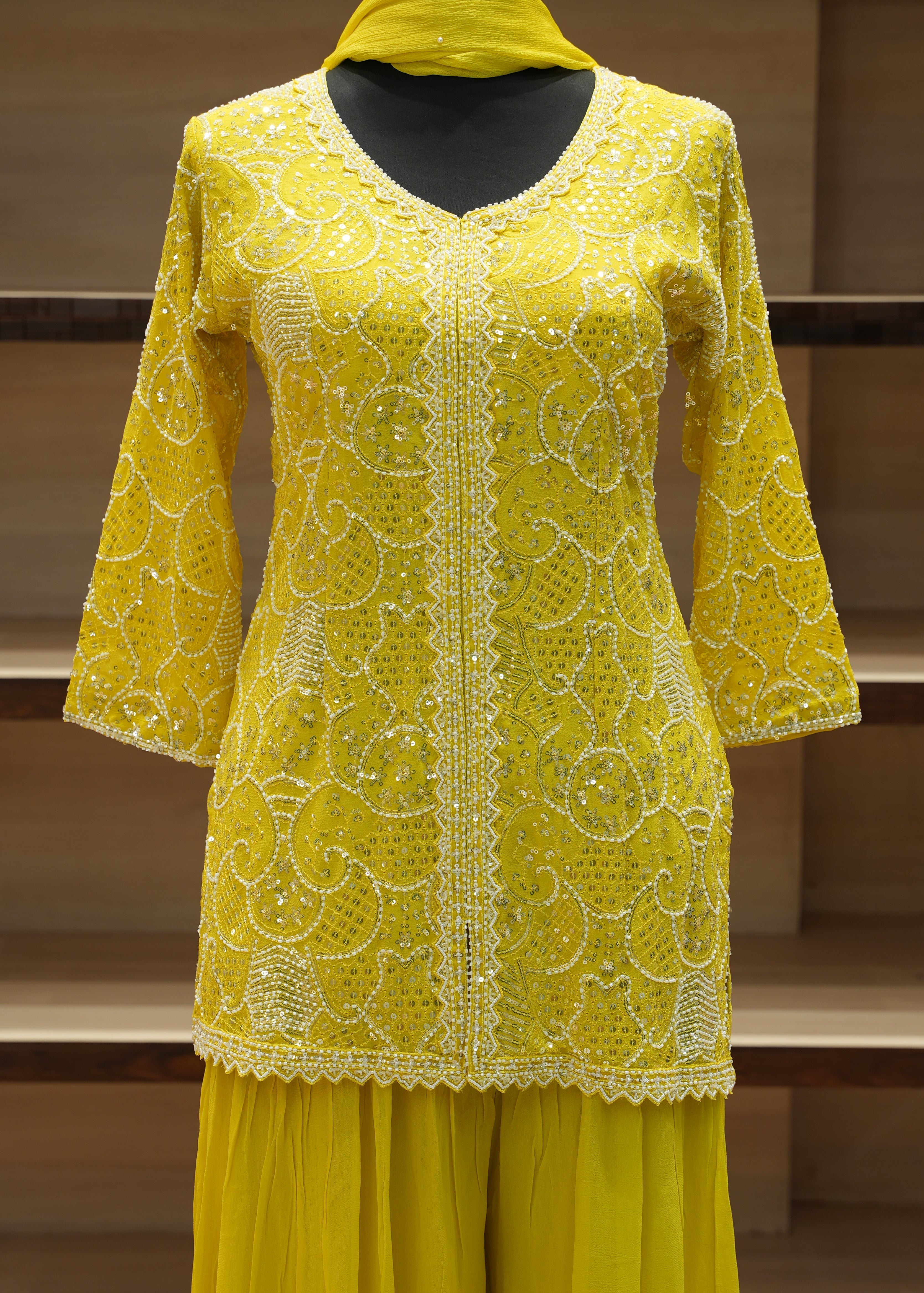 Yellow embroidered garment on a wooden stand against a neutral background