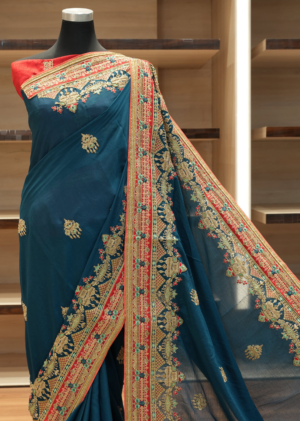 Blue saree with intricate gold and red patterns on a wooden stand.
