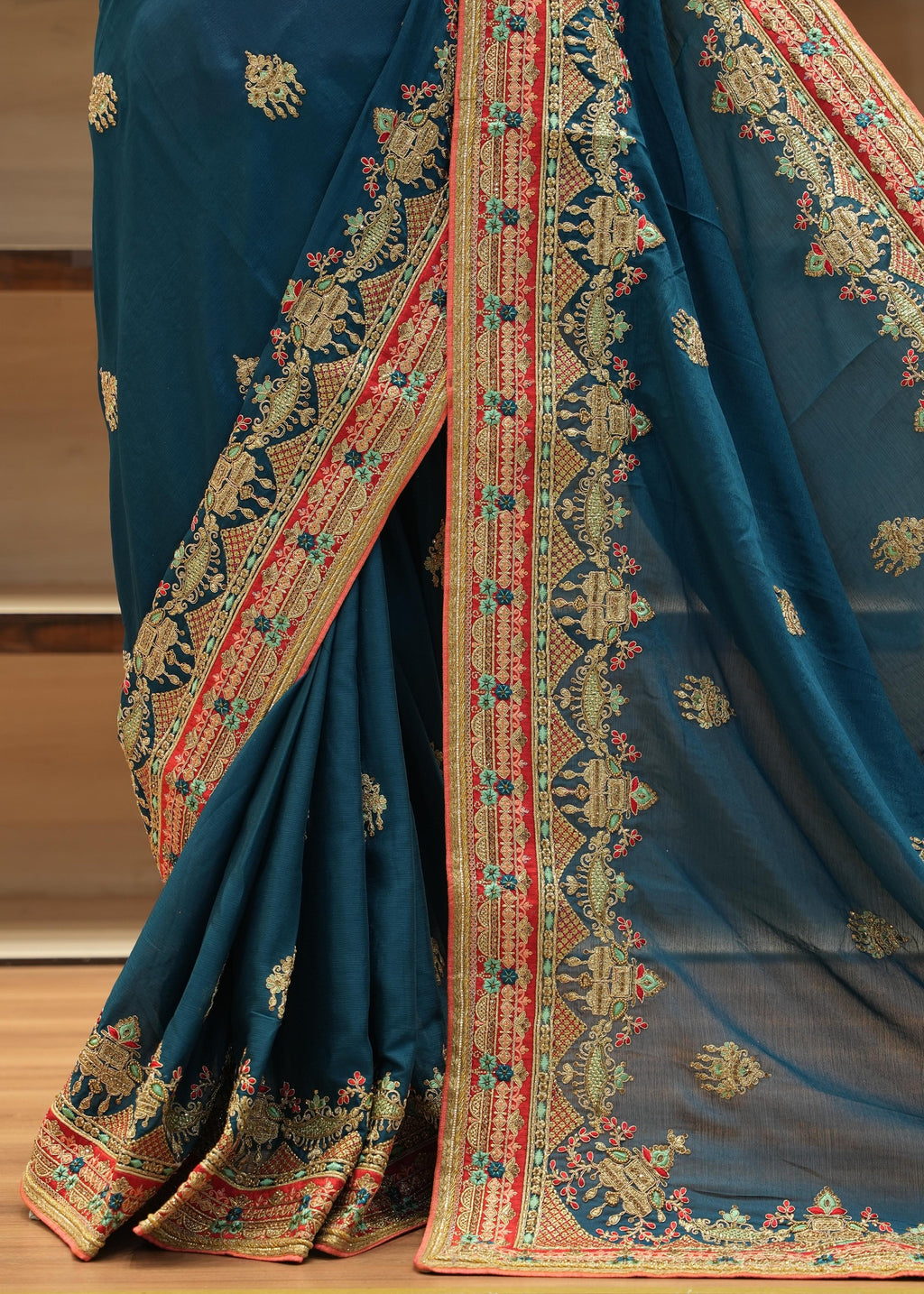 Blue saree with intricate gold and red patterns on a wooden floor.