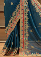 Blue saree with intricate gold and red patterns on a wooden floor.