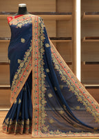 Navy blue saree with intricate gold and red patterns on a mannequin against a wooden background.
