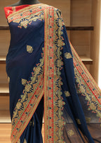 Navy blue saree with colorful embroidery on a wooden shelf.