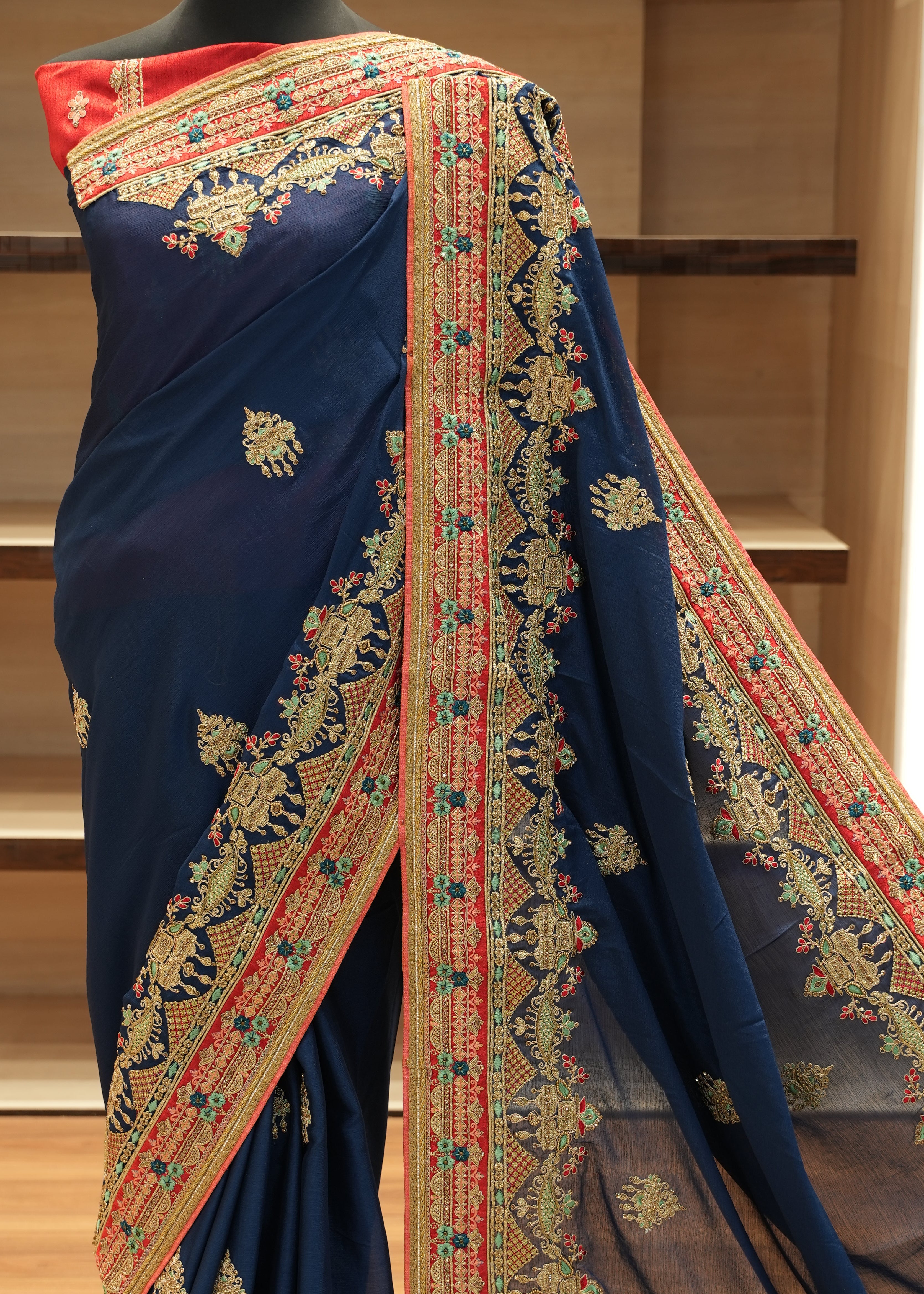 Navy blue saree with colorful embroidery on a wooden shelf.