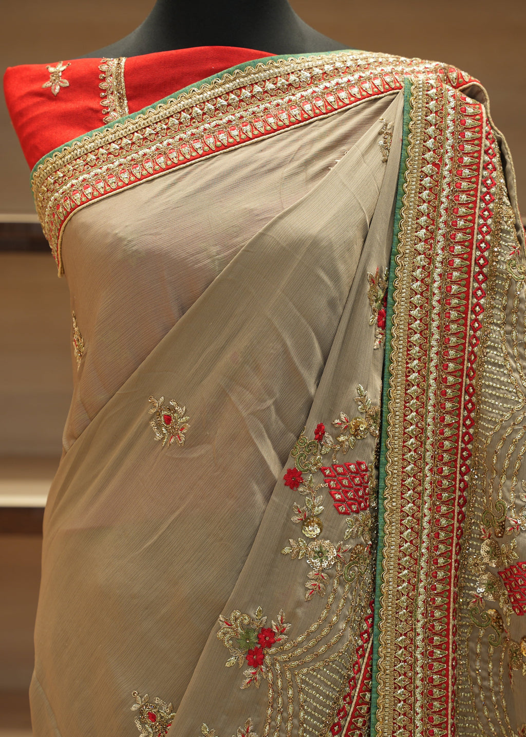 Beige saree with red and green embroidery on a mannequin against a neutral background