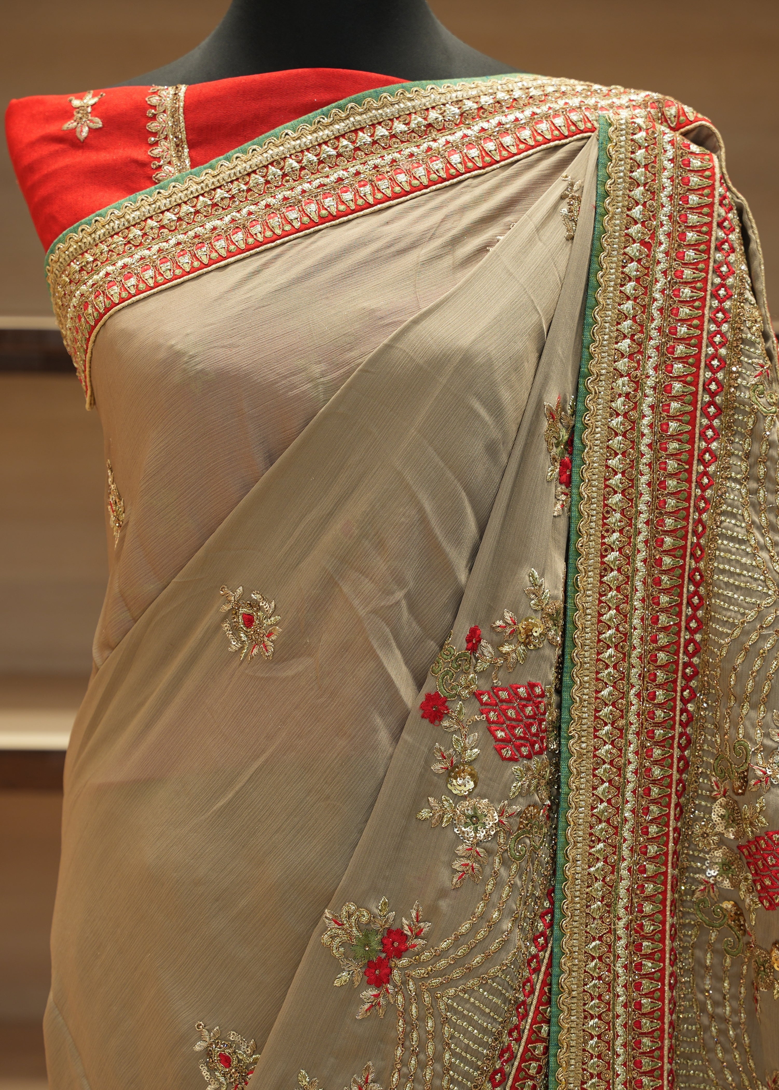 Beige saree with red and green embroidery on a mannequin against a neutral background