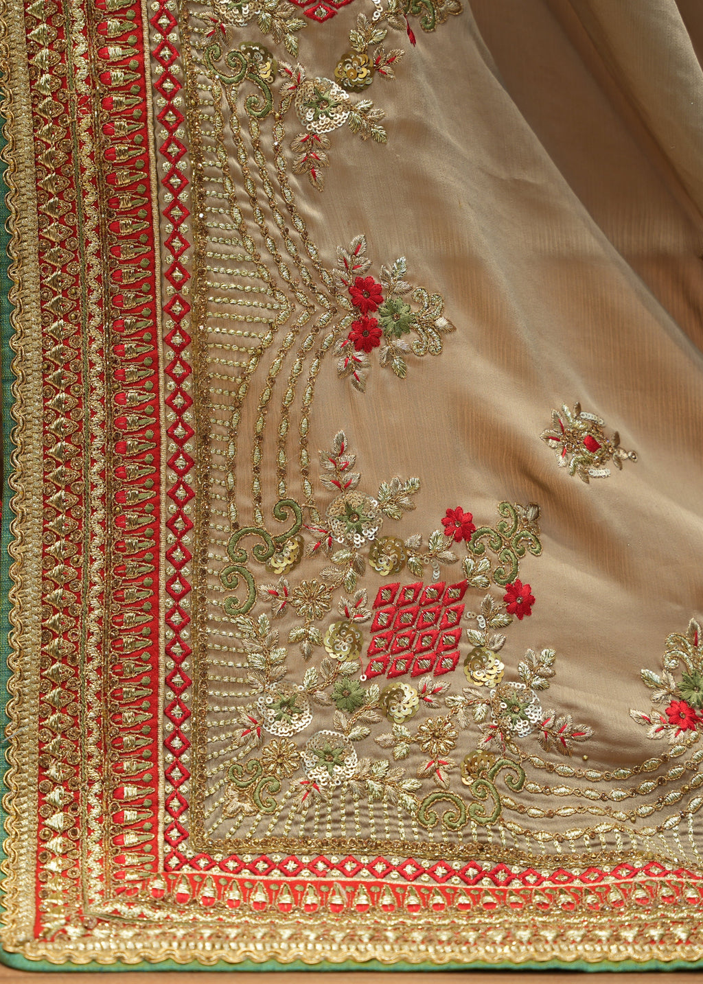 Close-up of a beige fabric with intricate red and gold embroidery on a wooden surface.