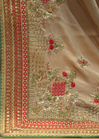 Close-up of a beige fabric with intricate red and gold embroidery on a wooden surface.