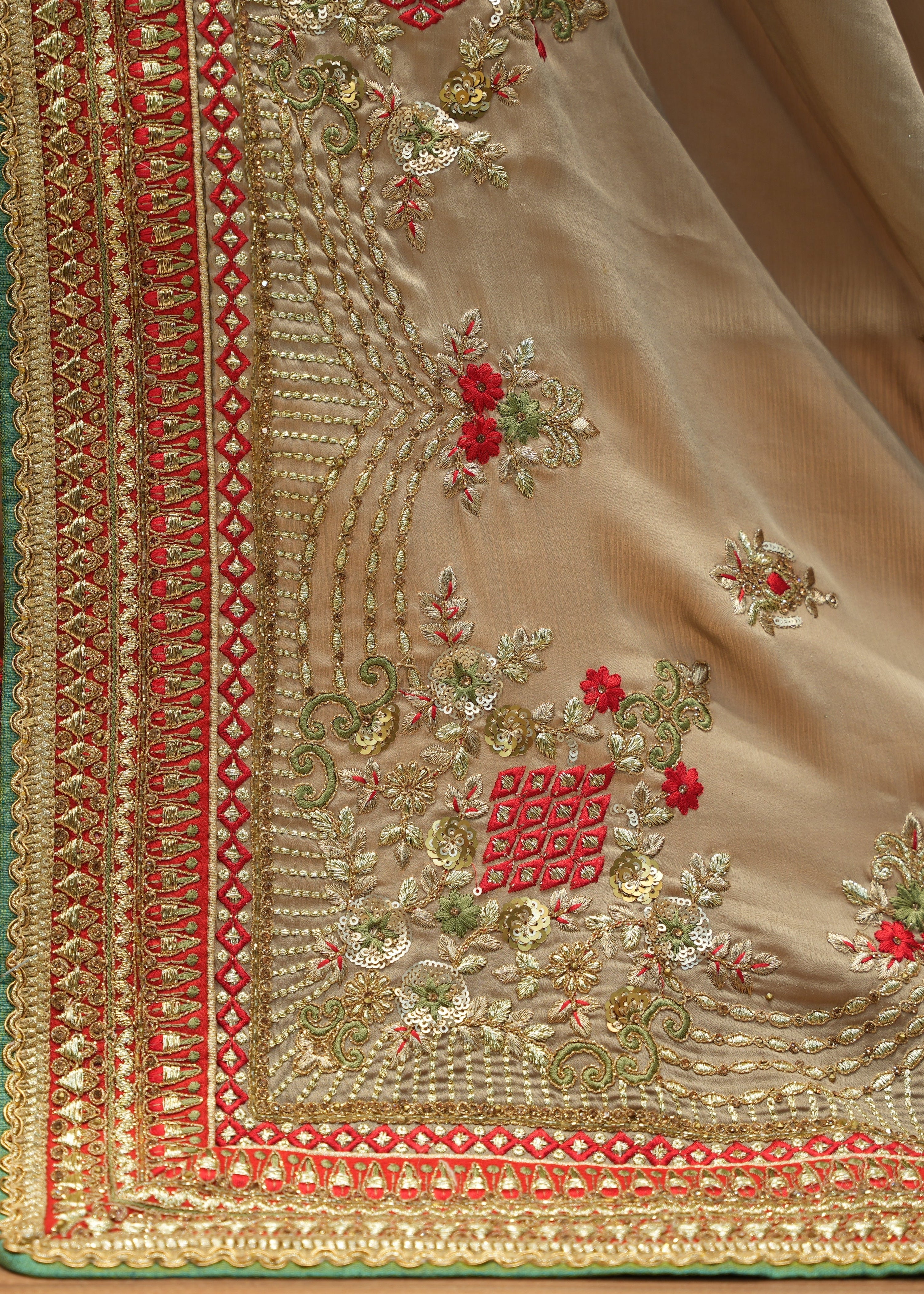 Close-up of a beige fabric with intricate red and gold embroidery on a wooden surface.