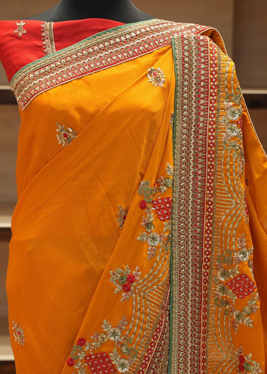 Orange saree with intricate gold and red embroidery on a mannequin against a neutral background