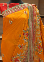 Orange saree with intricate gold and red embroidery on a mannequin against a neutral background