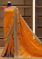 Orange saree with intricate patterns on a mannequin against a wooden background