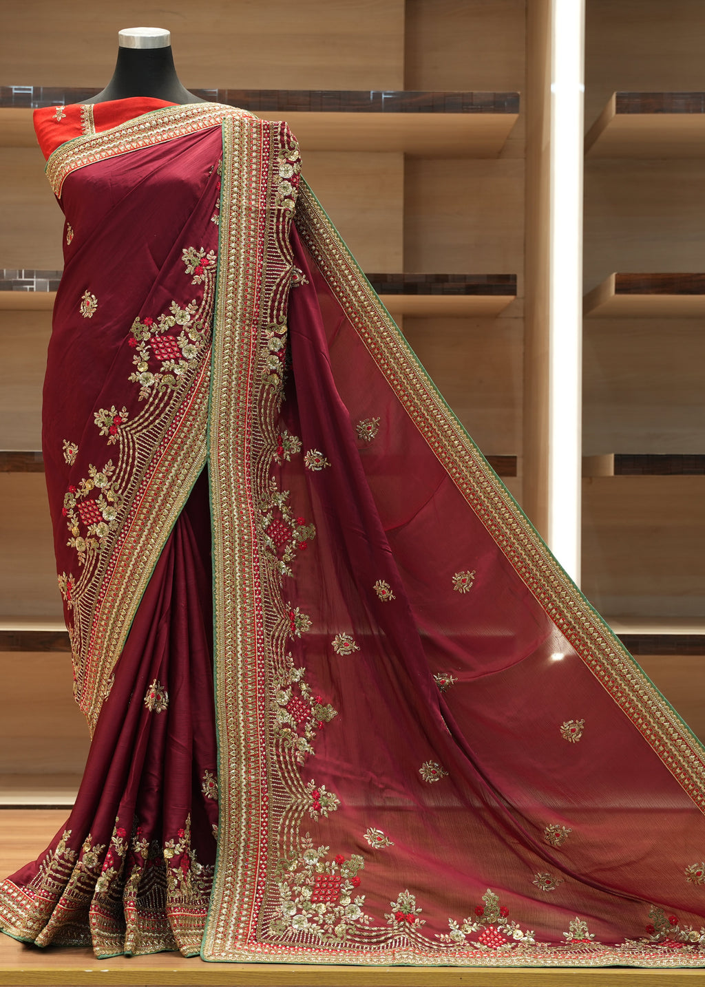 Maroon saree with gold embroidery on a mannequin against a wooden background