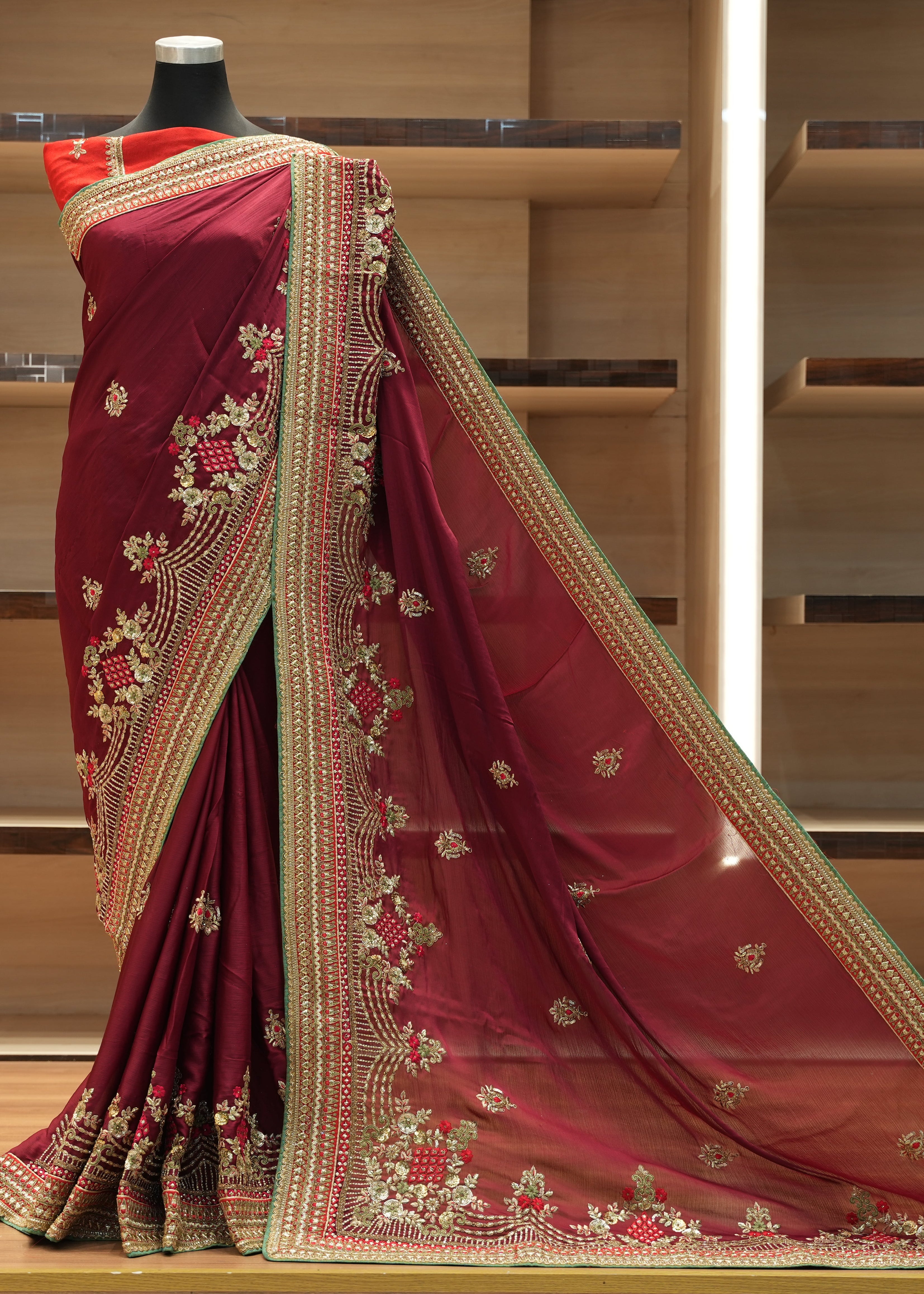Maroon saree with gold embroidery on a mannequin against a wooden background