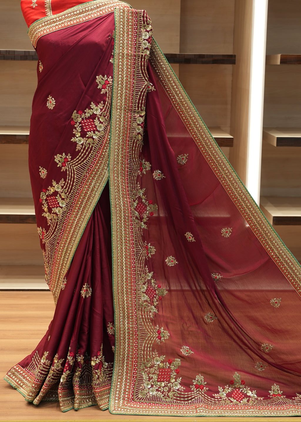 Red saree with gold embroidery on a wooden shelf