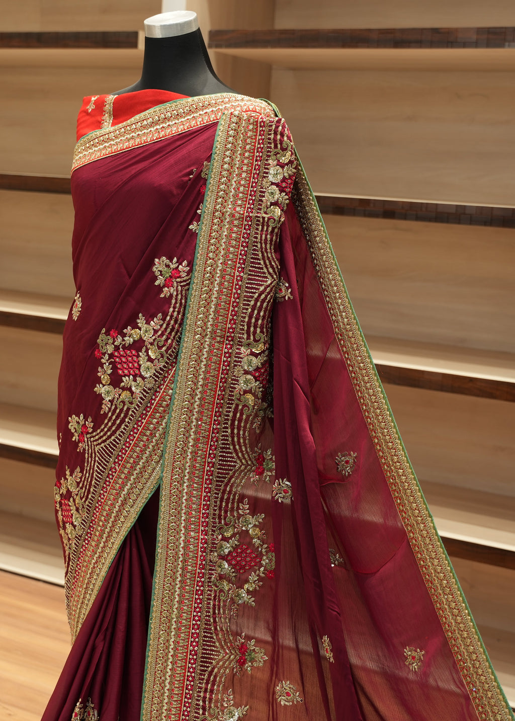 Maroon saree with gold embroidery on a mannequin against a wooden background