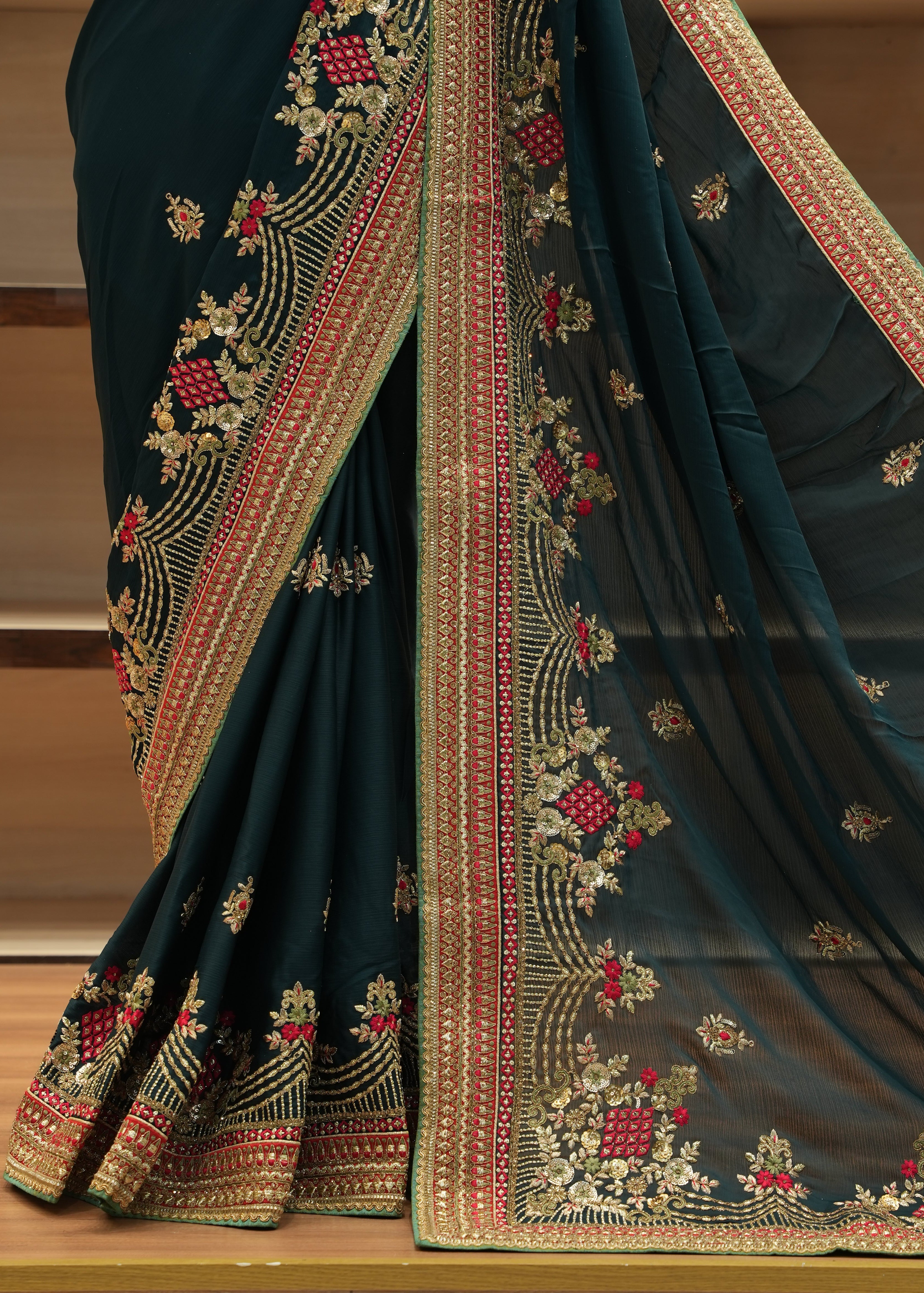 Dark green saree with intricate gold and red embroidery on a wooden surface