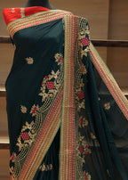 Dark green saree with red and gold border on a chair