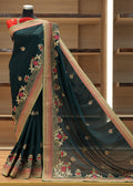 Dark green saree with intricate gold and red embroidery on a wooden shelf.