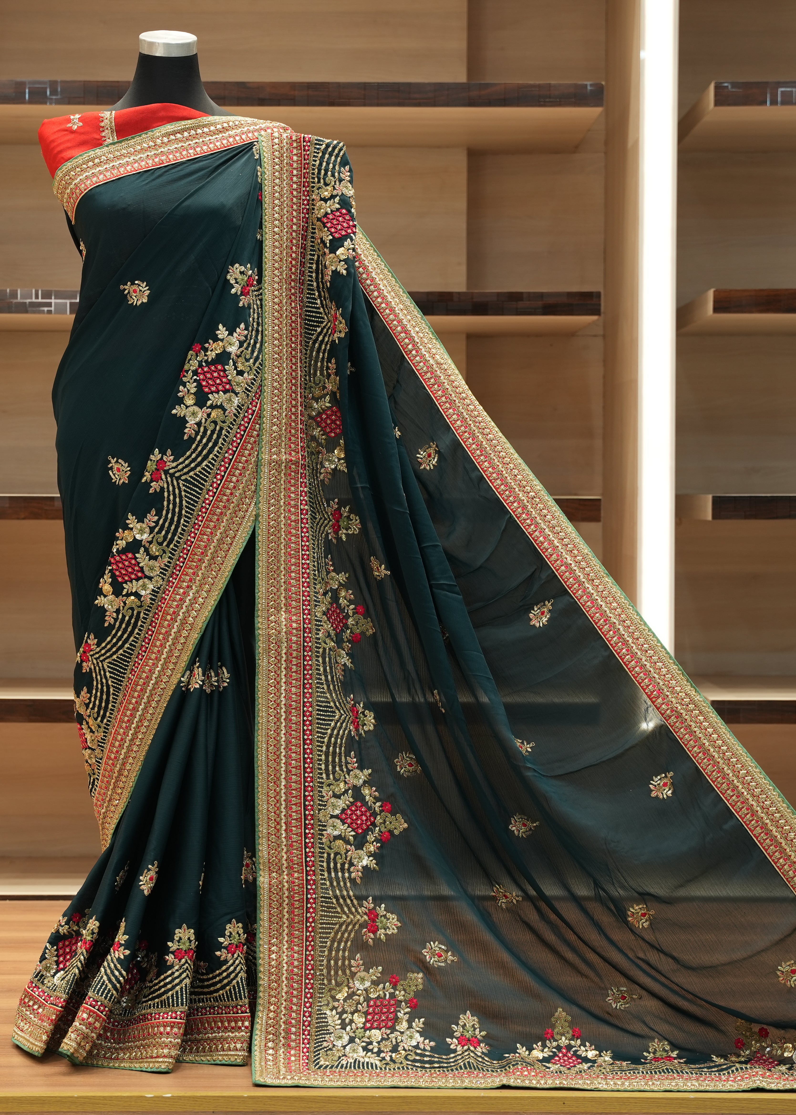 Dark green saree with intricate gold and red embroidery on a wooden shelf.