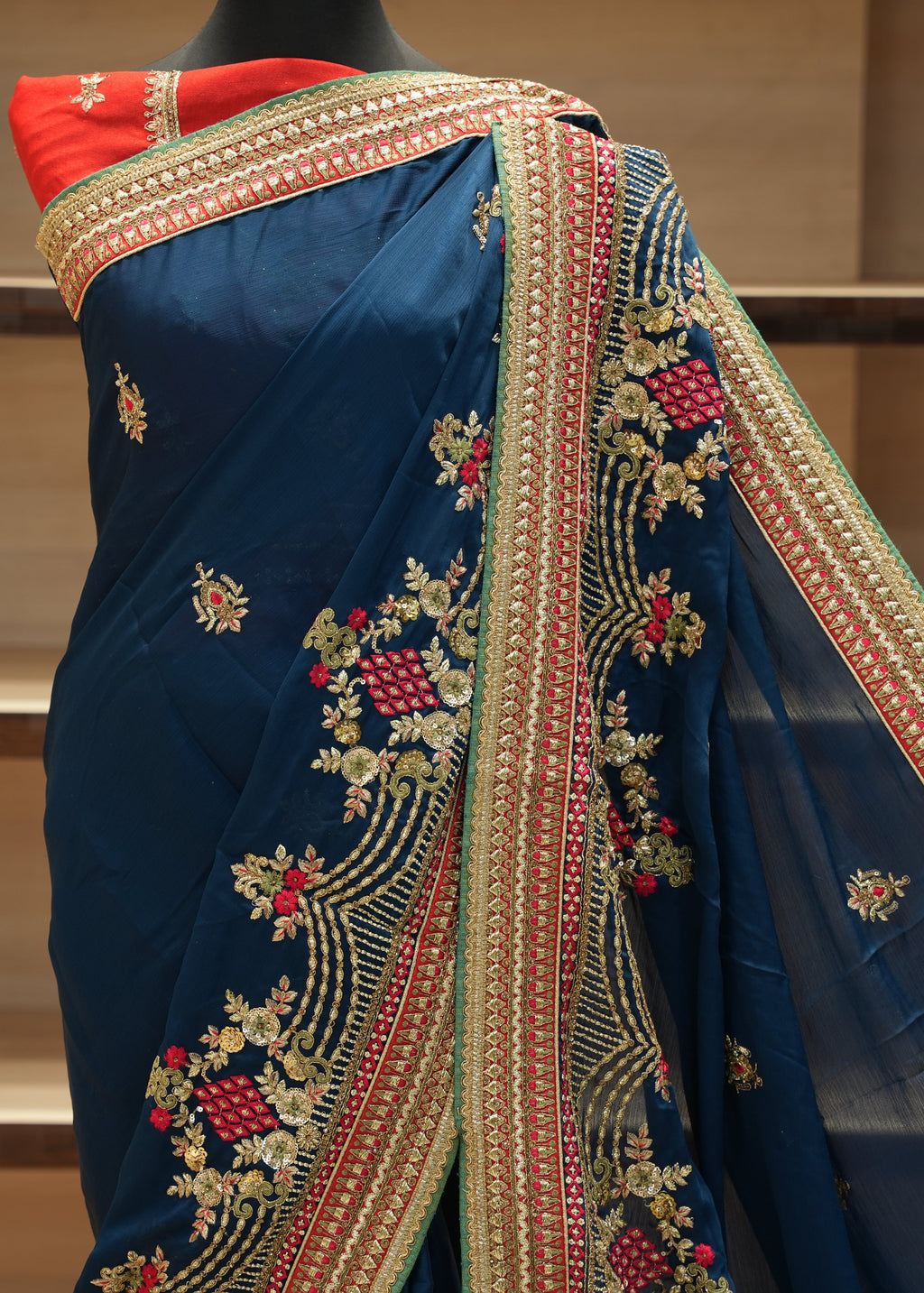 Blue saree with intricate gold and red embroidery on a wooden surface