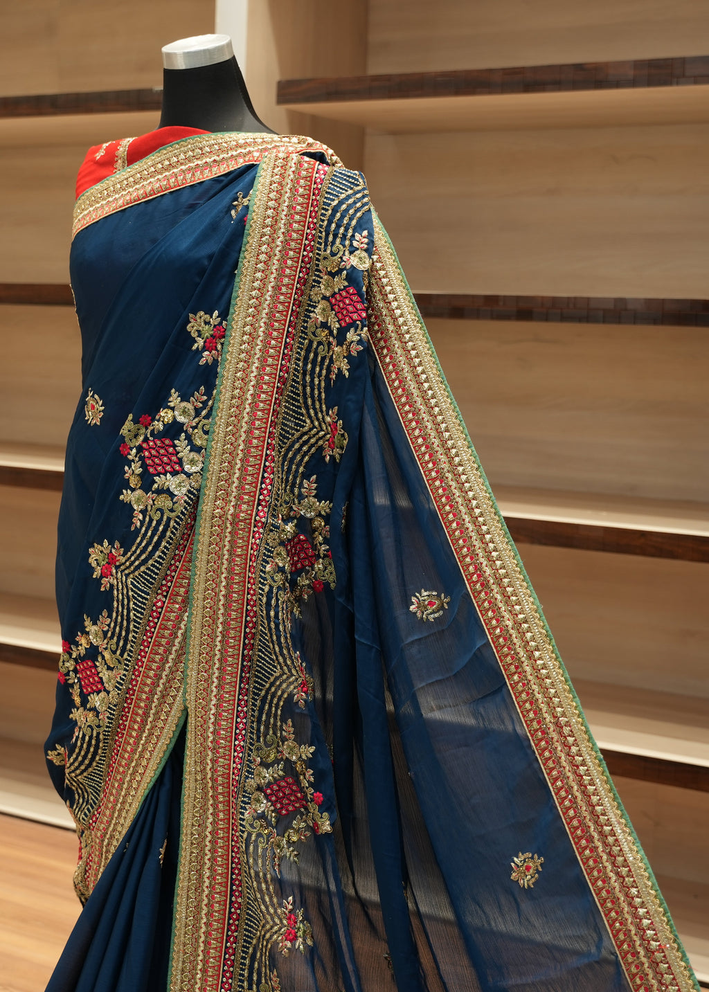 Blue saree with intricate gold embroidery on a mannequin against a wooden shelf background