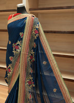 Blue saree with intricate gold embroidery on a mannequin against a wooden shelf background