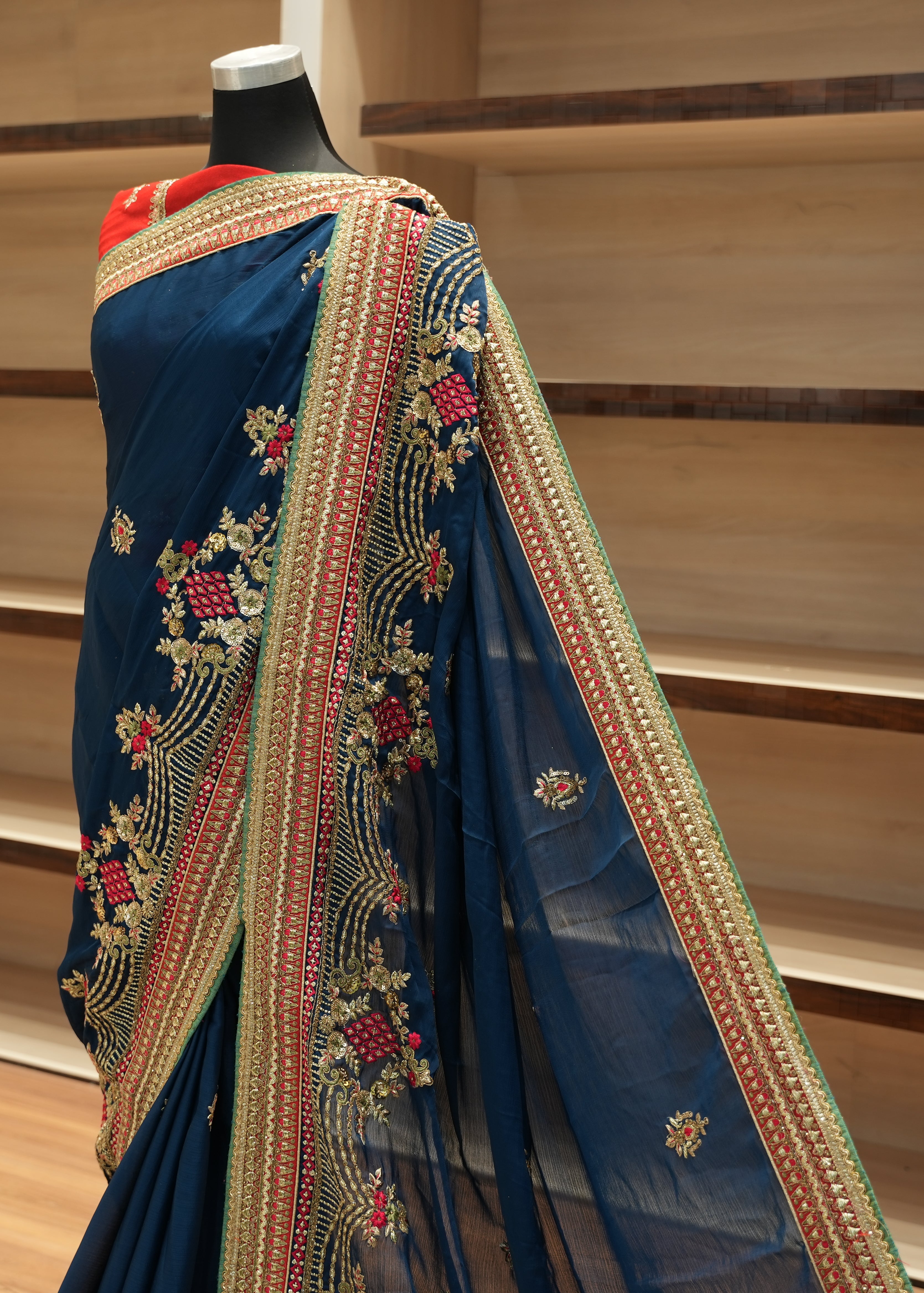 Blue saree with intricate gold embroidery on a mannequin against a wooden shelf background