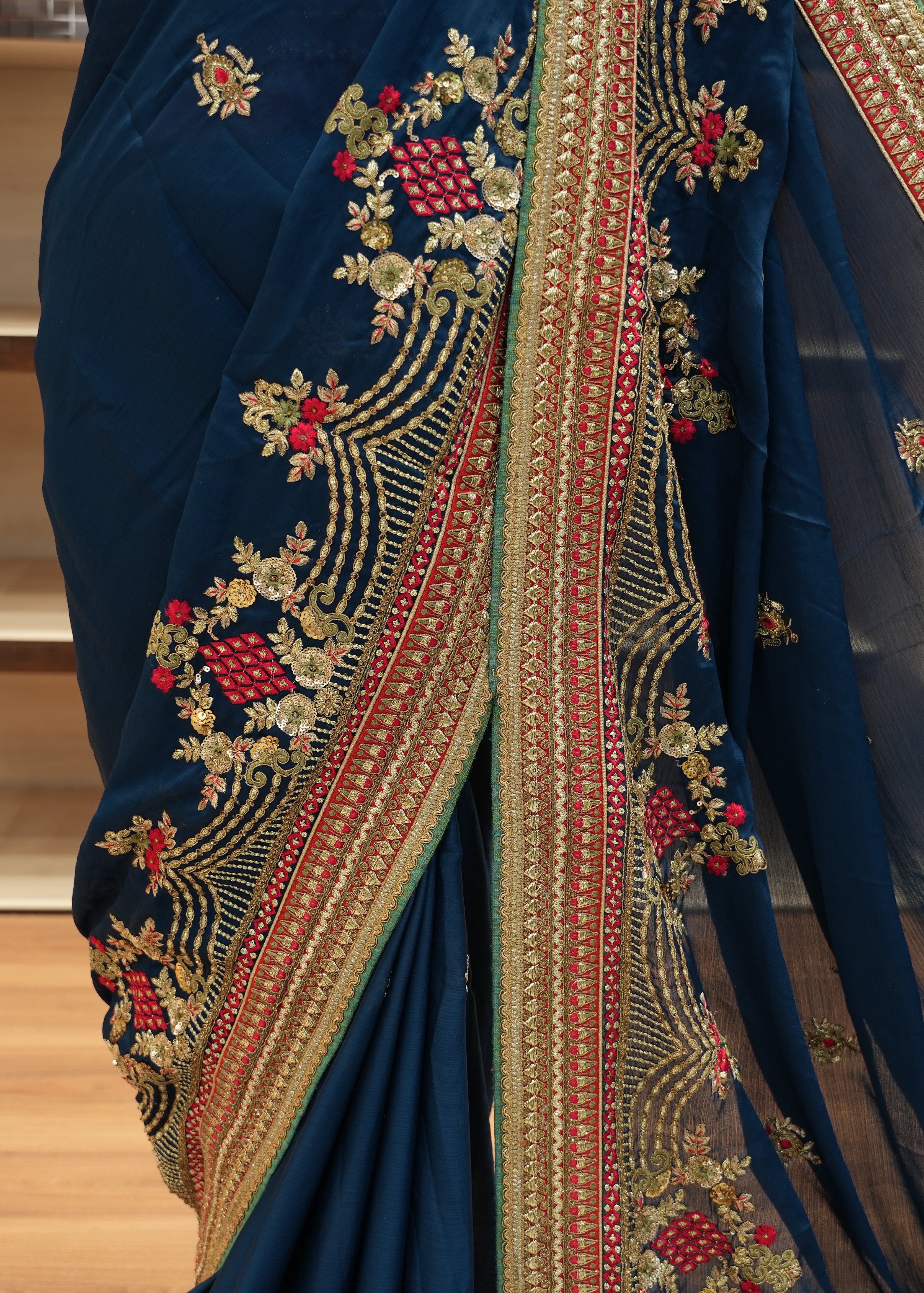 Blue saree with intricate gold and red embroidery on a wooden surface