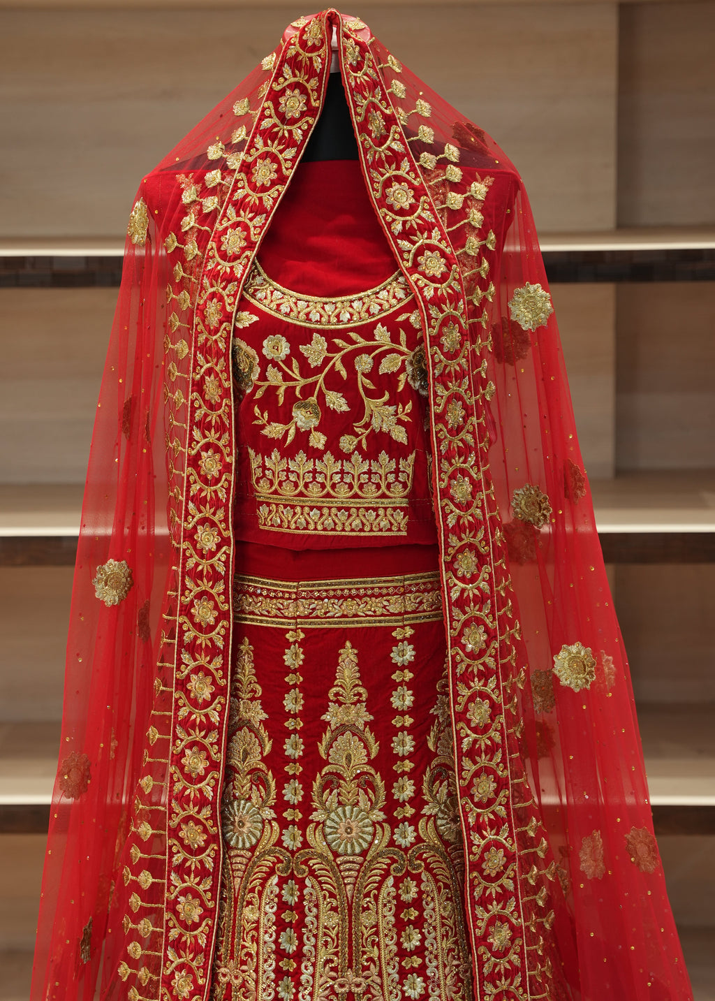 Red fabric with gold embroidery on a stand against a neutral background
