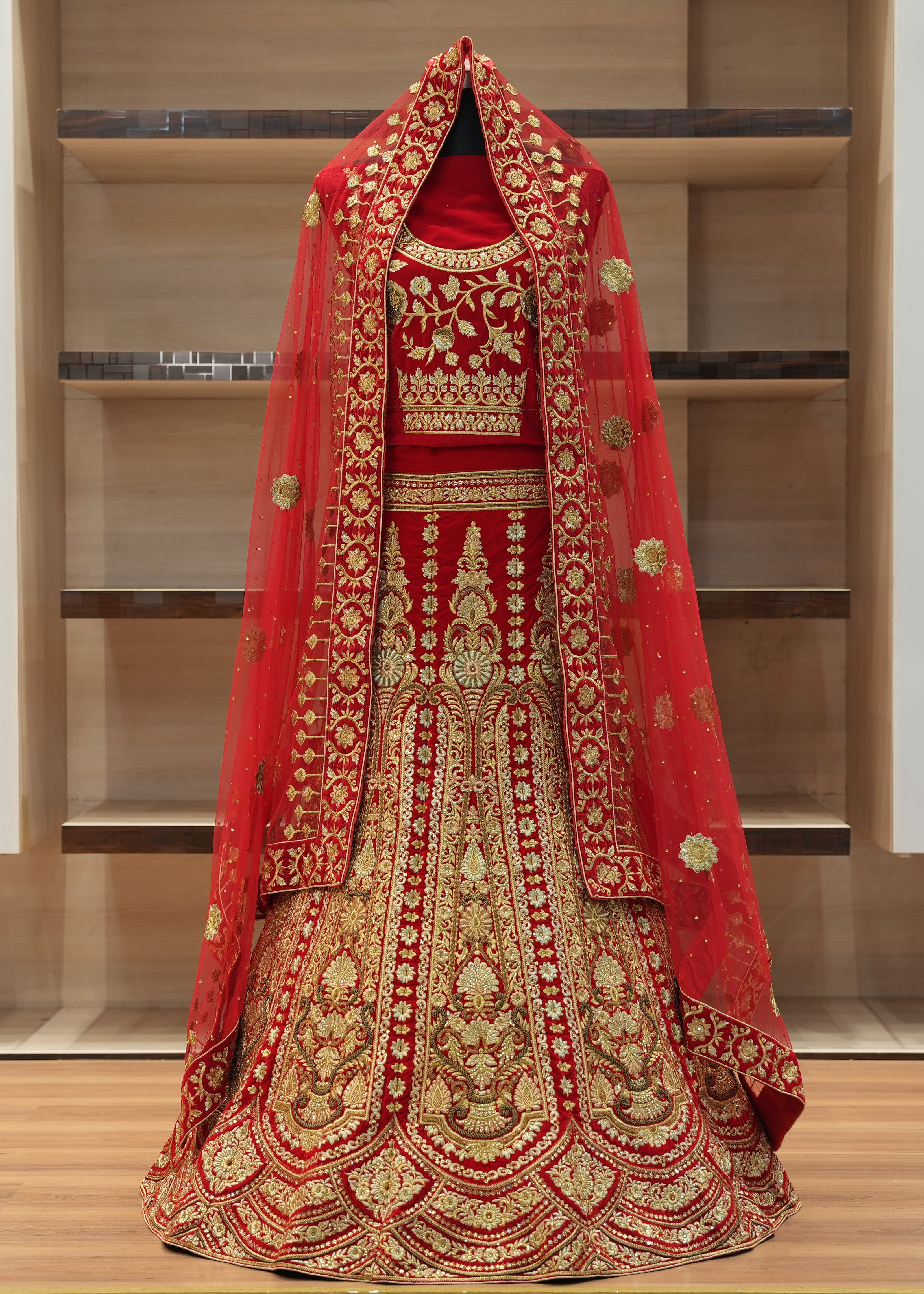 Red and gold embroidered traditional outfit on a wooden floor with shelves in the background