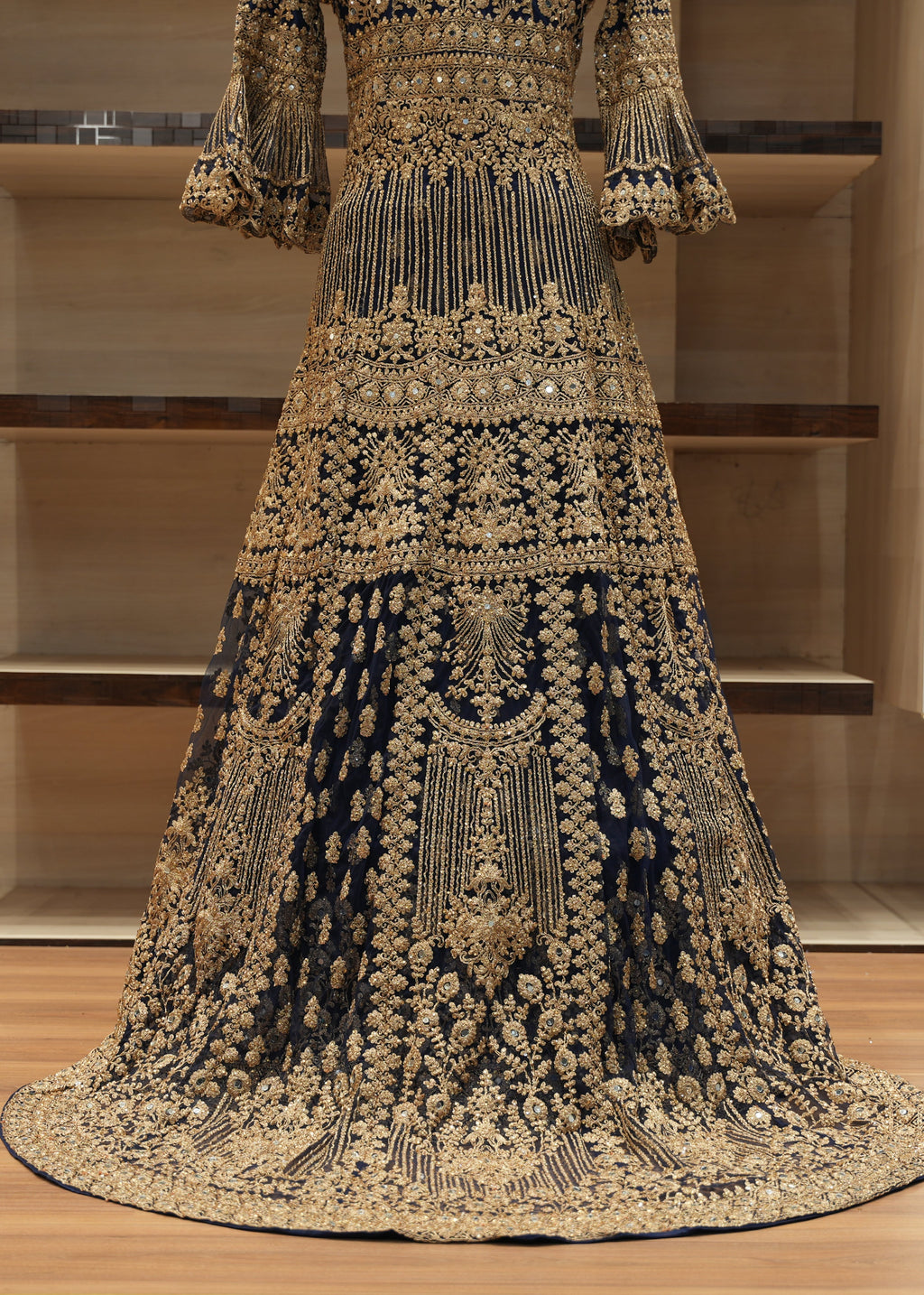 Elaborately embroidered traditional dress on a wooden floor with shelves in the background