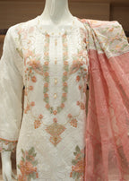 Embroidered white and pink traditional outfit on a mannequin with a blurred indoor background.