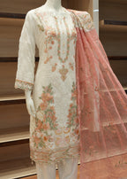 Traditional embroidered outfit on a mannequin with a pink dupatta in front of a wooden panel.