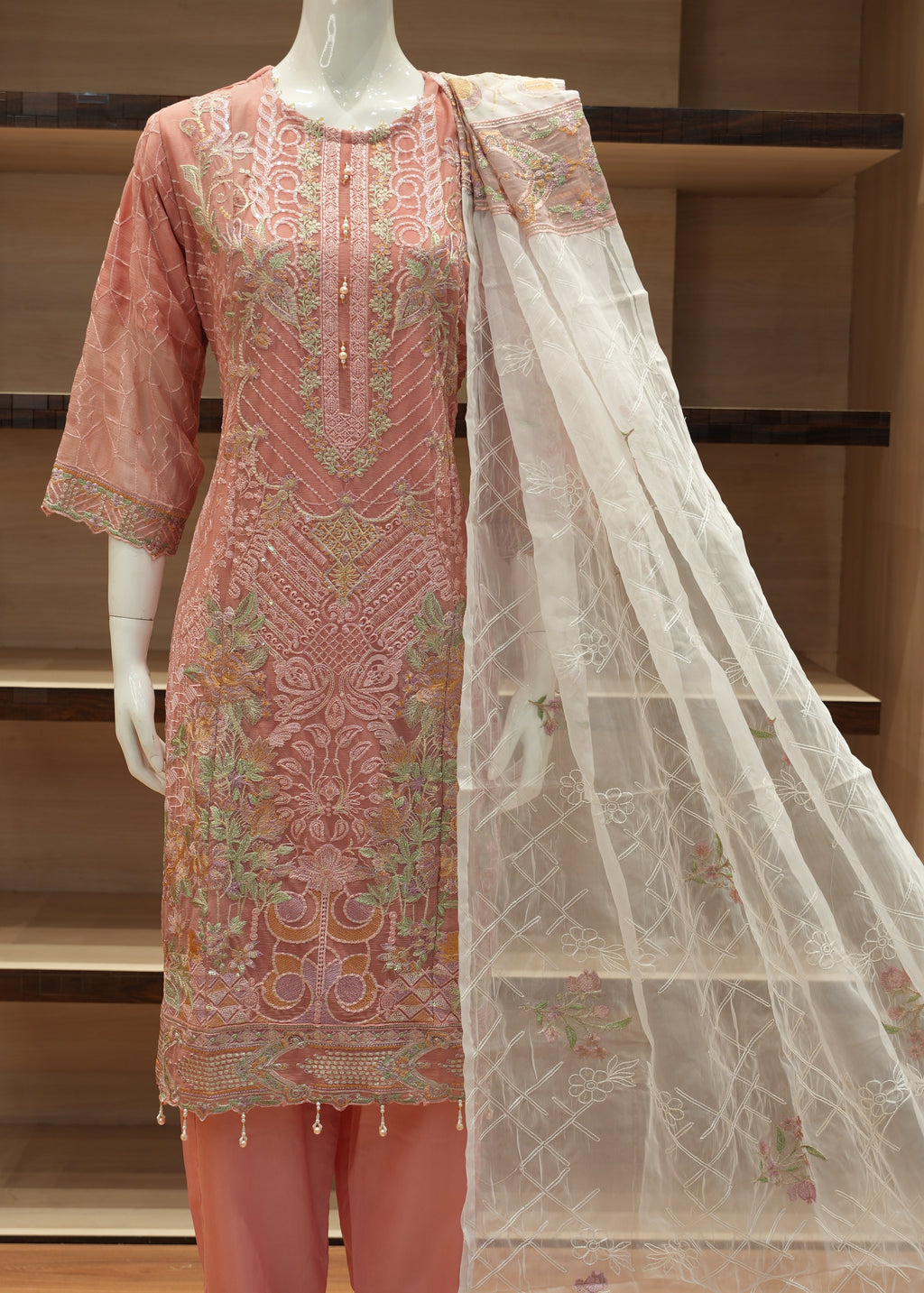 Decorative pink fabric with intricate patterns on a mannequin against a wooden shelf background.