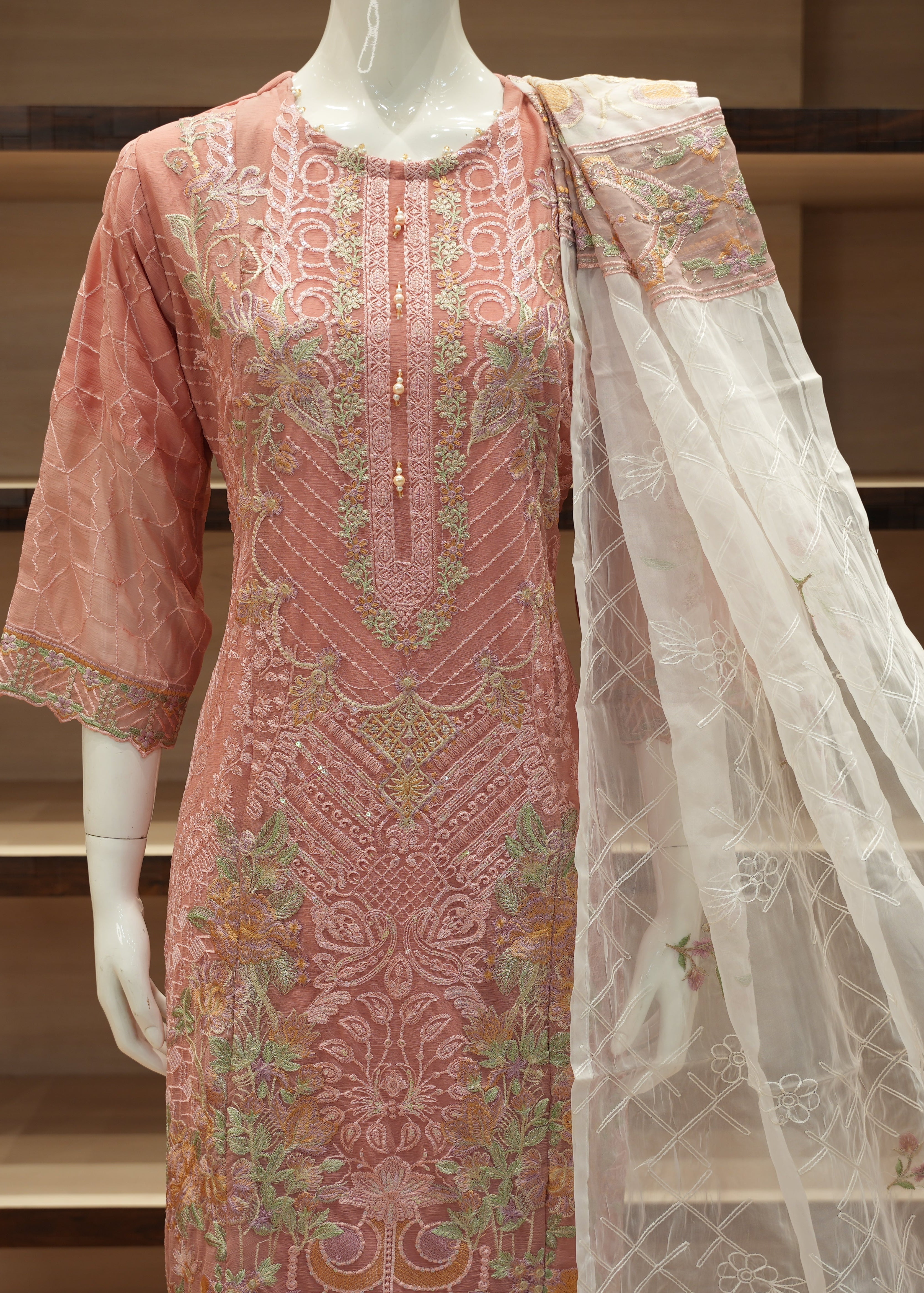 Pink embroidered dress with a white dupatta on a mannequin against a wooden shelf background