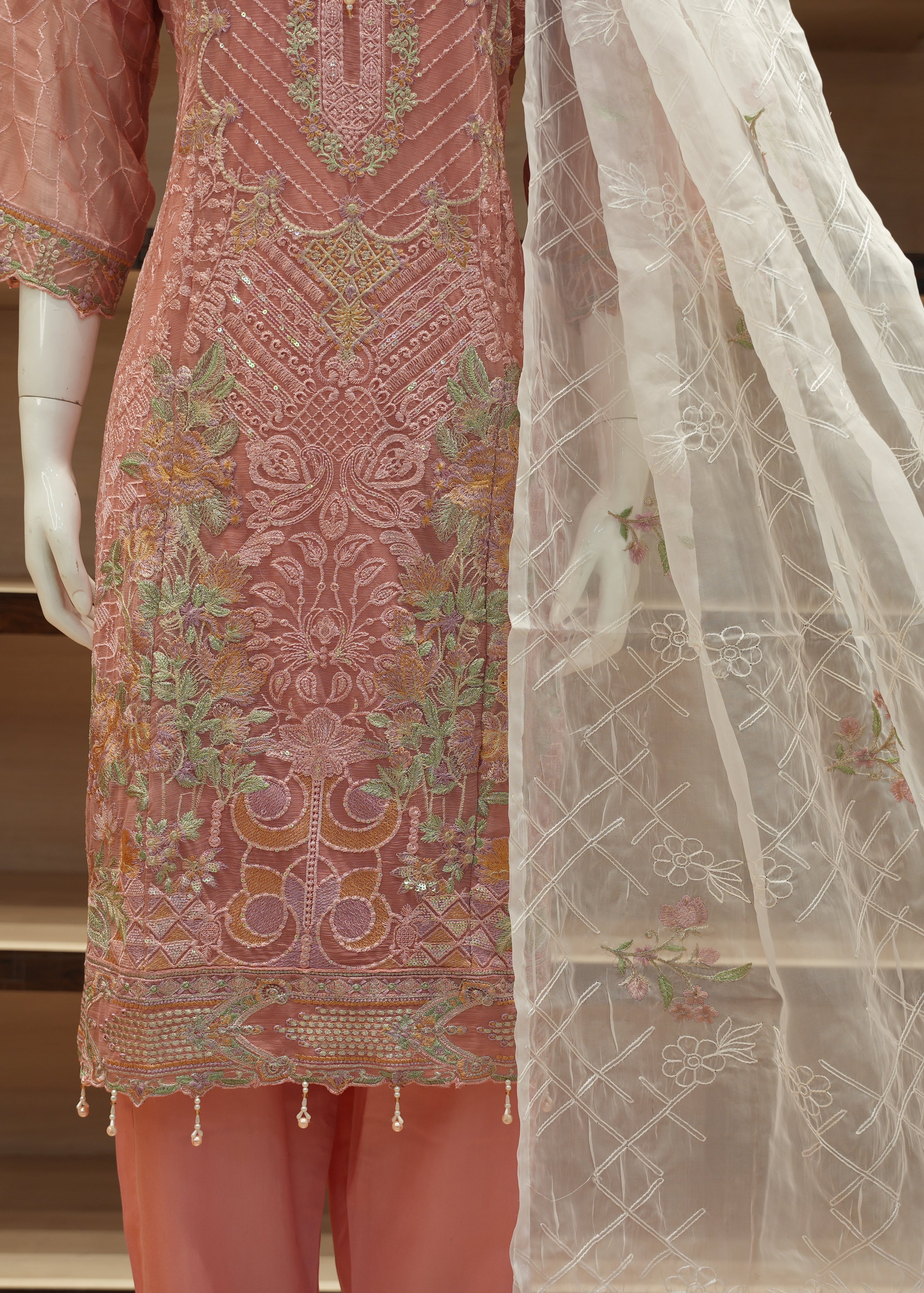 Embroidered pink and white traditional outfit on a mannequin with a neutral background