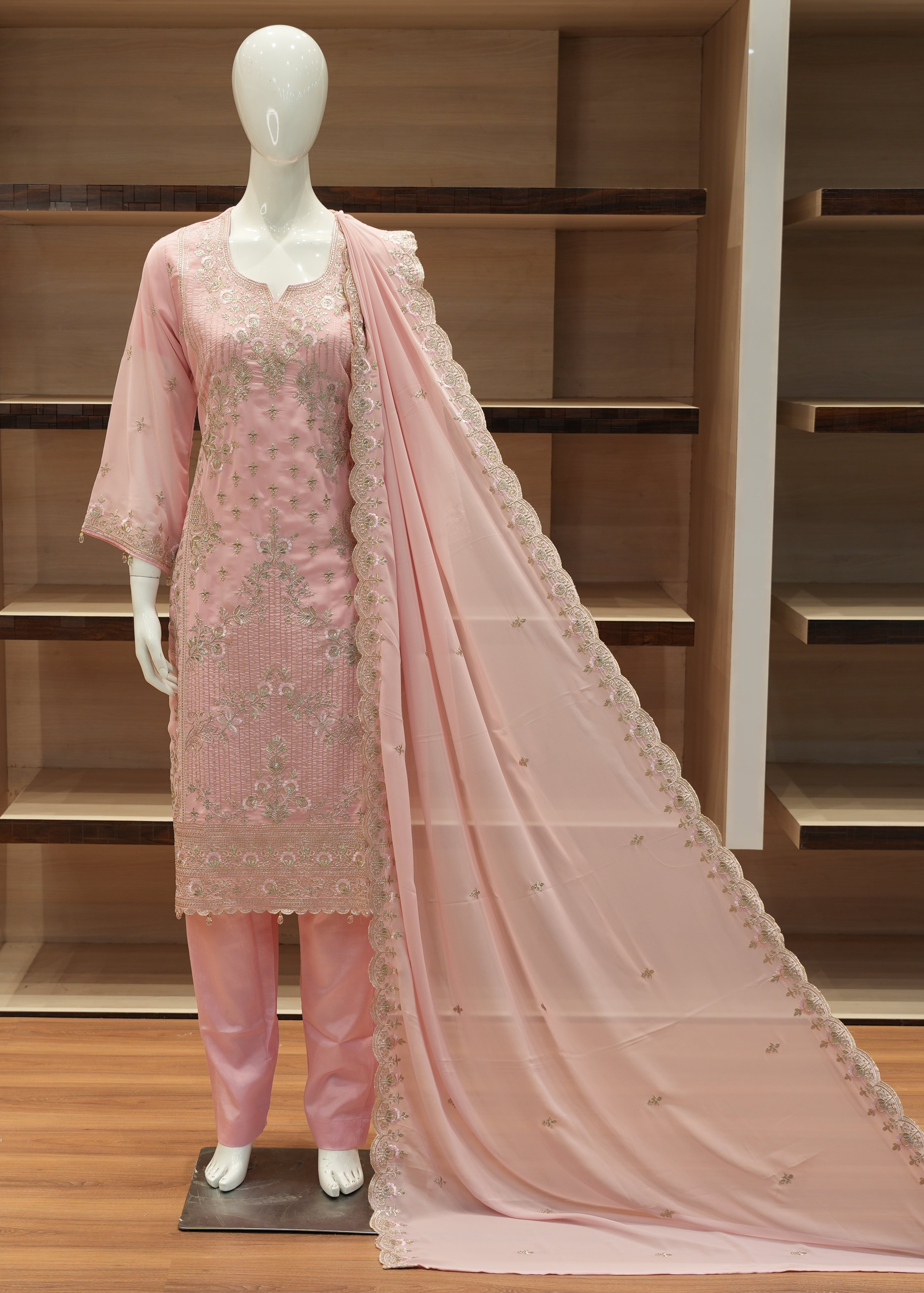 Mannequin wearing a pink embroidered outfit with a matching dupatta on a wooden floor.