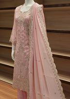 Pink fabric with intricate embroidery draped over a wooden surface