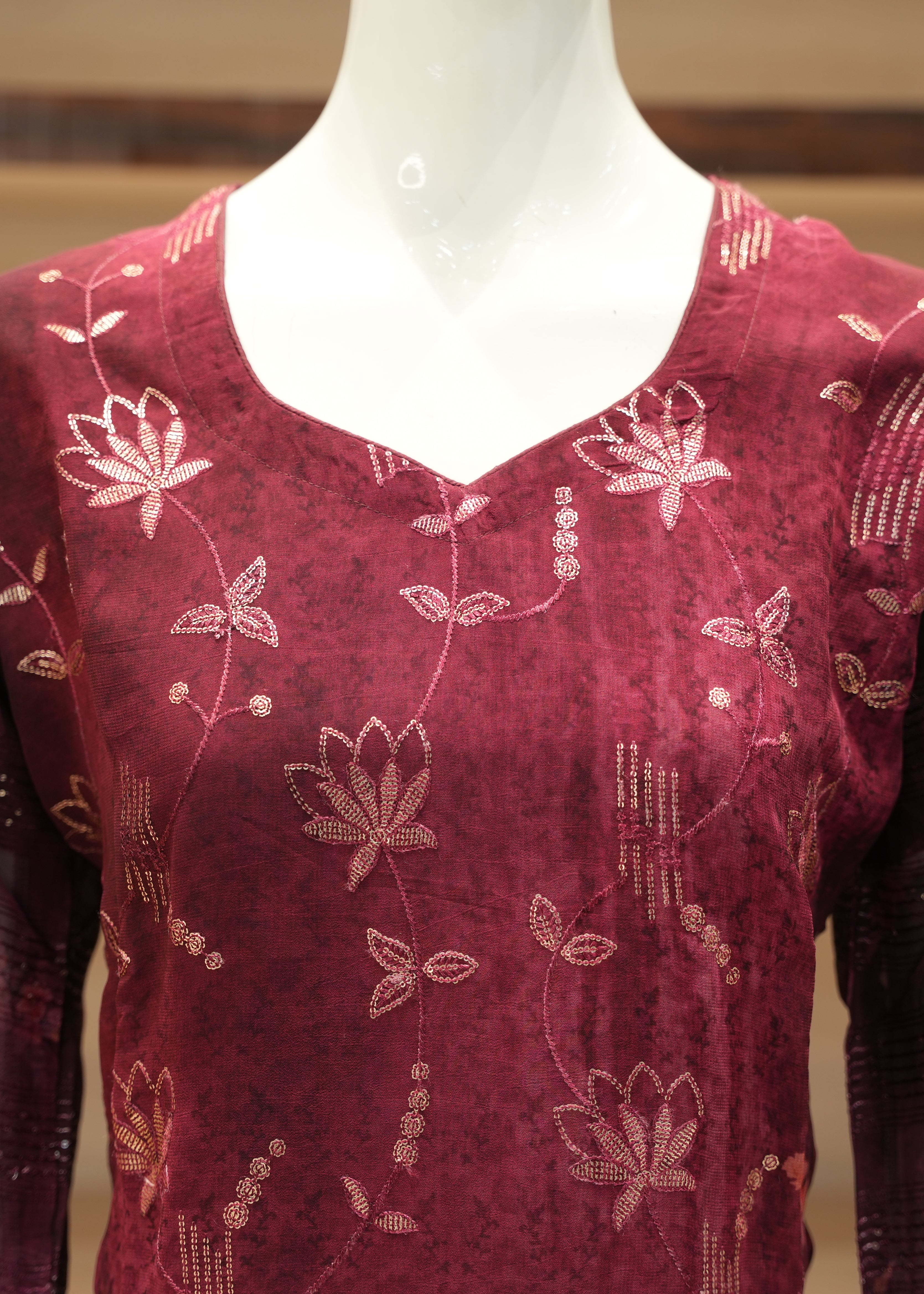 Maroon top with floral patterns on a mannequin against a blurred background