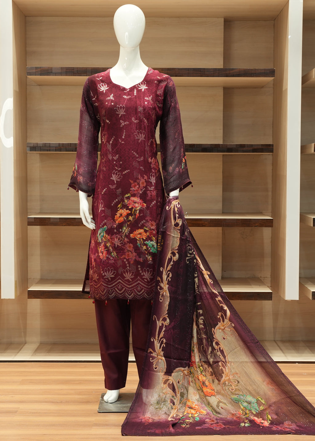 Mannequin wearing a maroon traditional outfit with floral patterns in a wooden display cabinet.