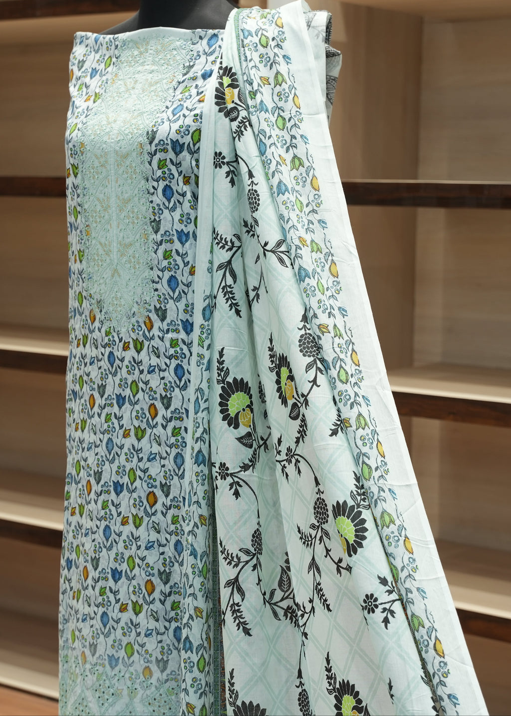 Mannequin wearing a light blue floral dress against wooden shelves
