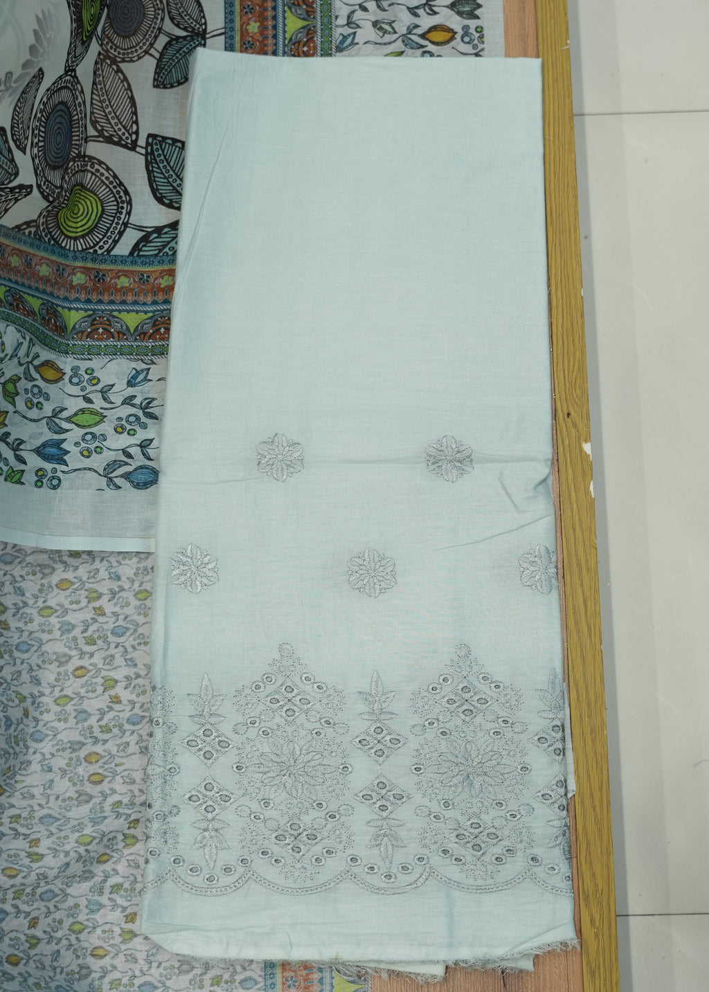 White fabric with intricate black patterns on a wooden surface with a patterned background