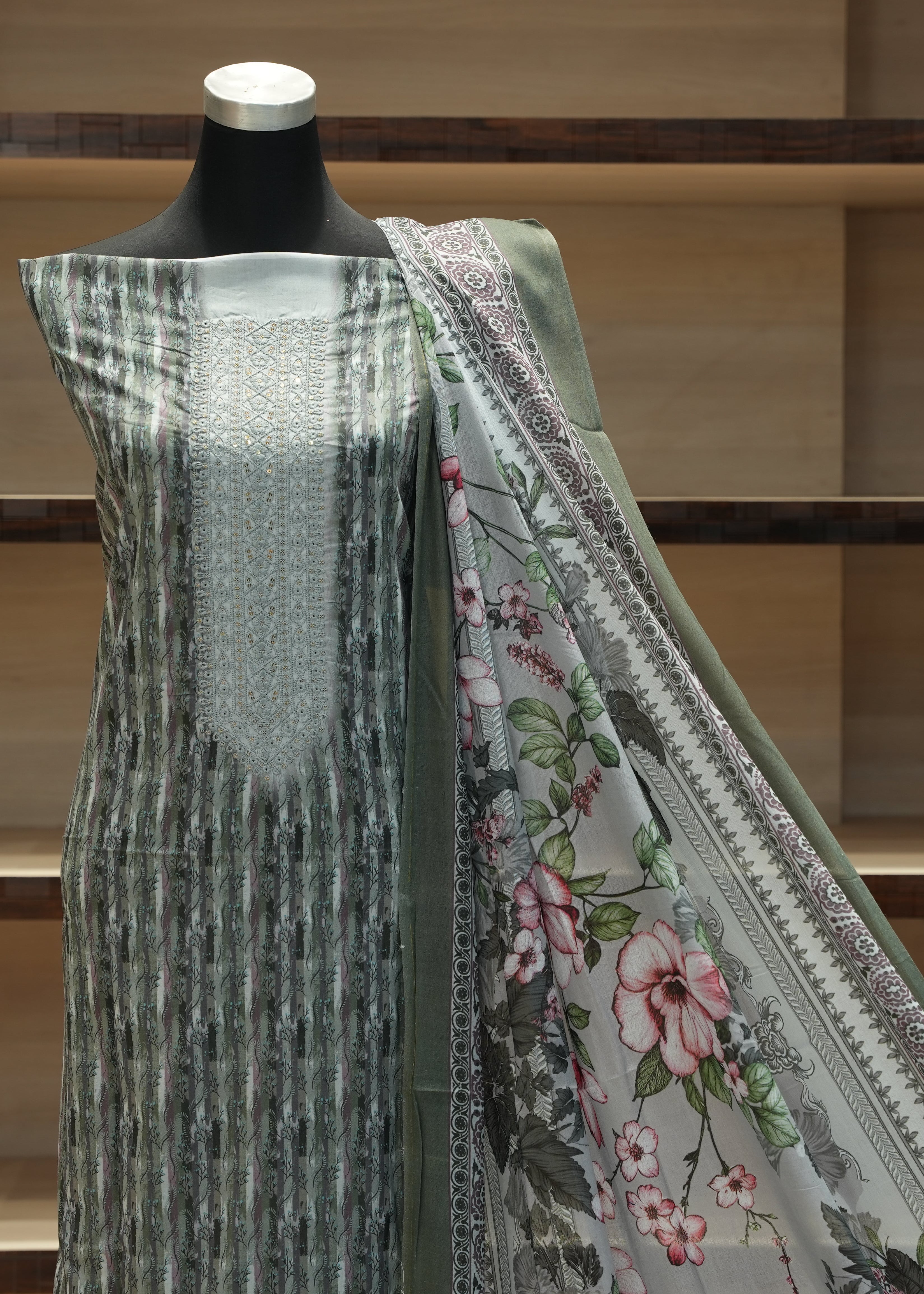 Mannequin wearing a traditional outfit with a floral shawl against a wooden shelf background