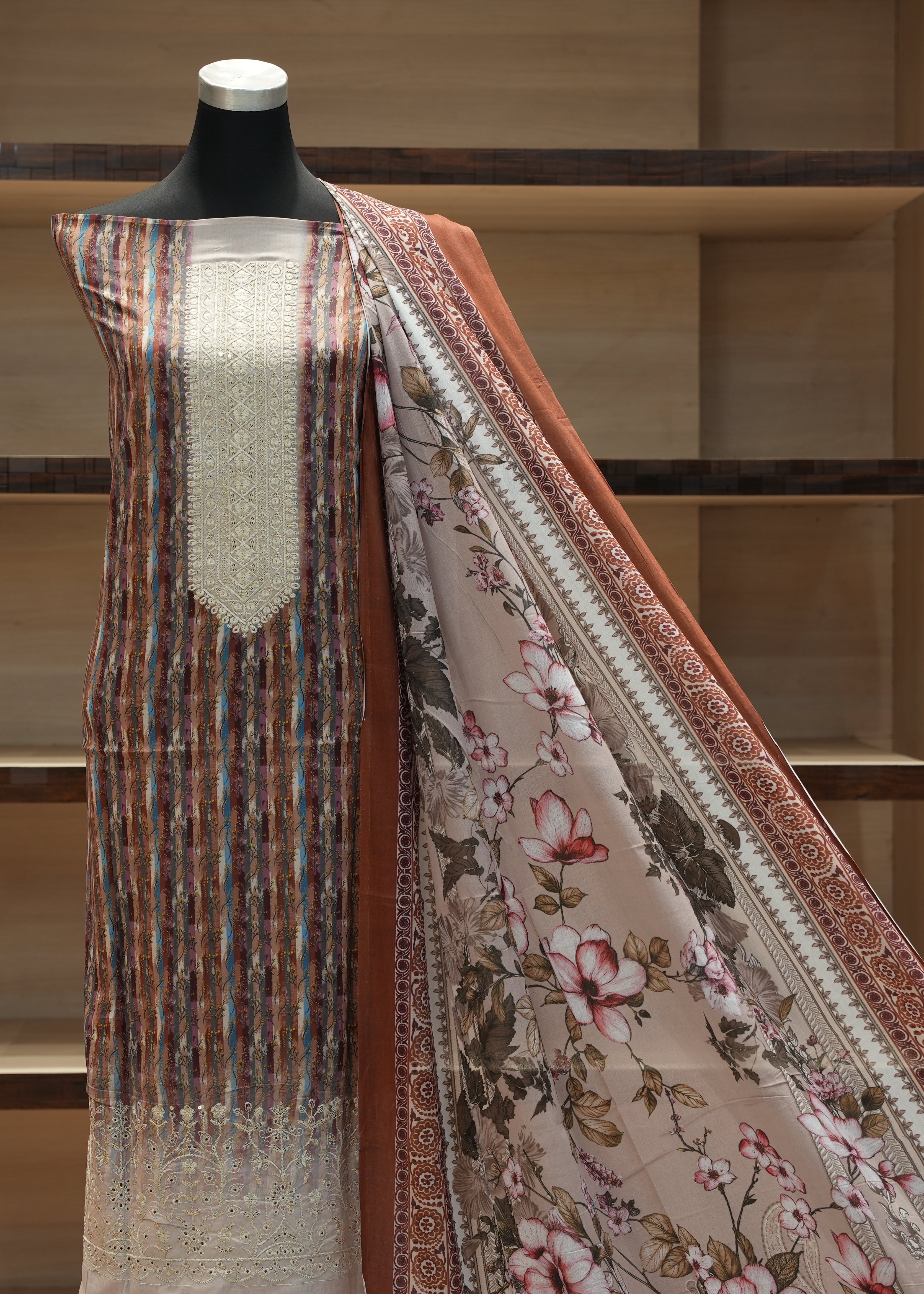 Mannequin wearing a floral-patterned fabric with a plain fabric draped over it against a wooden shelf background.